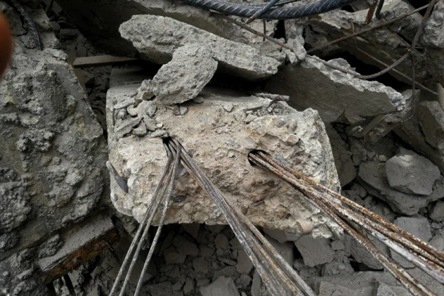 Broken concrete of a collapsed truss with open tendon ducts, bundles of bare, corroded prestressing wires running out of them and no grout around them